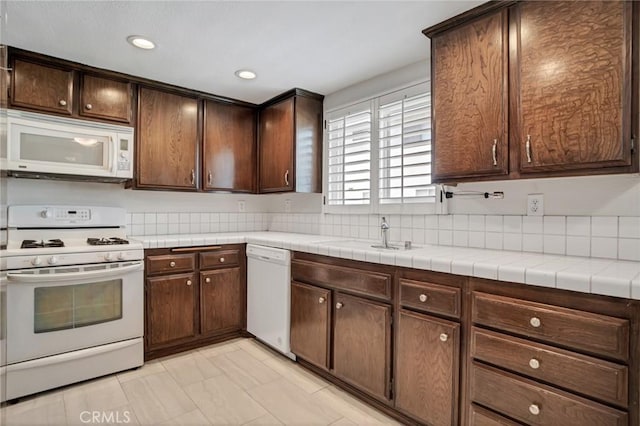 kitchen featuring white appliances, dark brown cabinets, recessed lighting, and a sink
