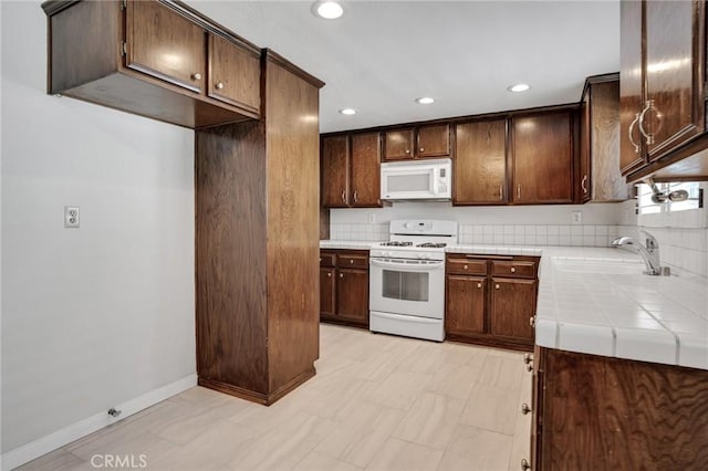 kitchen with dark brown cabinetry, a sink, white appliances, tile countertops, and recessed lighting