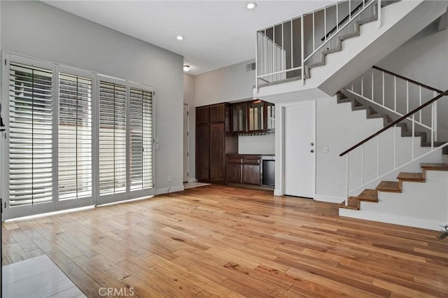 unfurnished living room featuring light wood-type flooring, recessed lighting, baseboards, and stairway