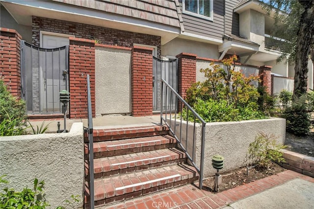 property entrance featuring brick siding, a gate, and stucco siding