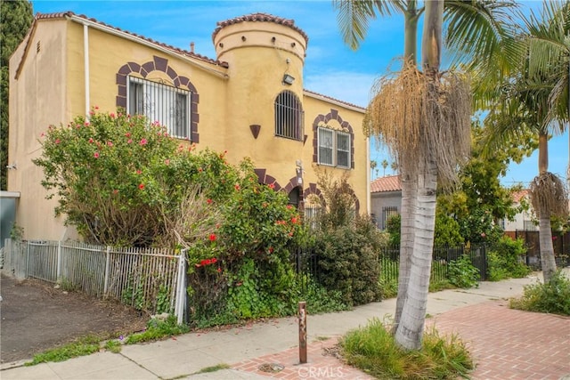 mediterranean / spanish house with stucco siding, a tile roof, and fence