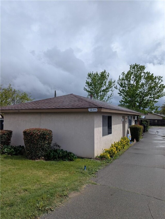 view of home's exterior featuring roof with shingles, stucco siding, and a yard