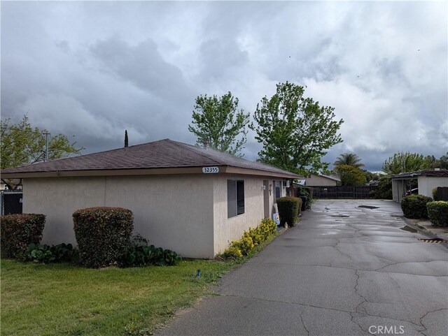 view of home's exterior featuring roof with shingles, stucco siding, driveway, and fence