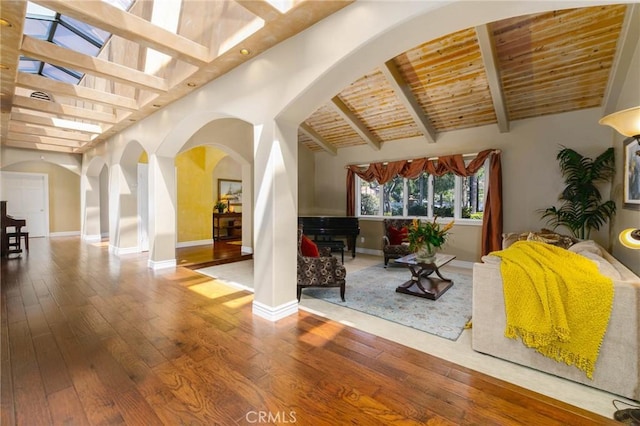 living area with beam ceiling, hardwood / wood-style floors, baseboards, wood ceiling, and arched walkways