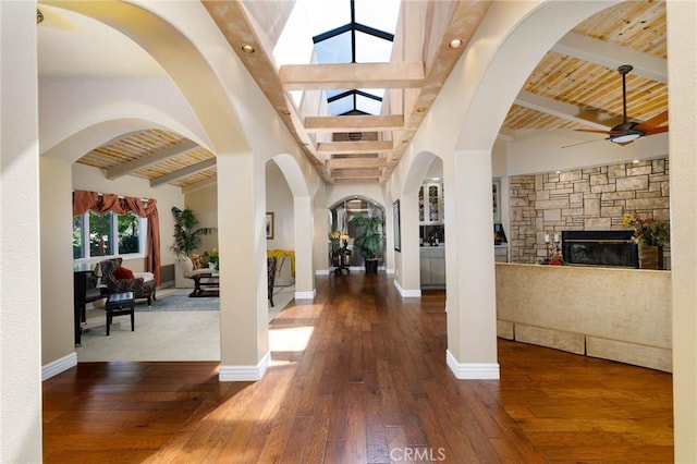 entrance foyer with wood-type flooring, a fireplace, beamed ceiling, ceiling fan, and a skylight