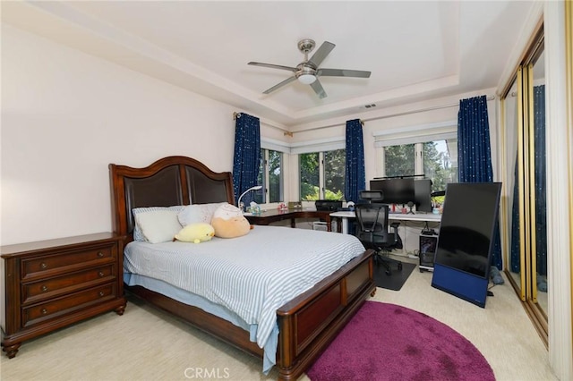 bedroom with a tray ceiling, visible vents, light carpet, and ceiling fan