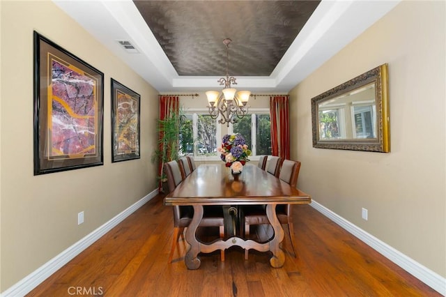 dining space featuring a chandelier, baseboards, wood finished floors, a tray ceiling, and visible vents