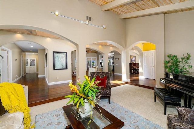 living room featuring visible vents, wood finished floors, beamed ceiling, baseboards, and arched walkways