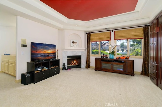 carpeted living area with a tiled fireplace and a tray ceiling