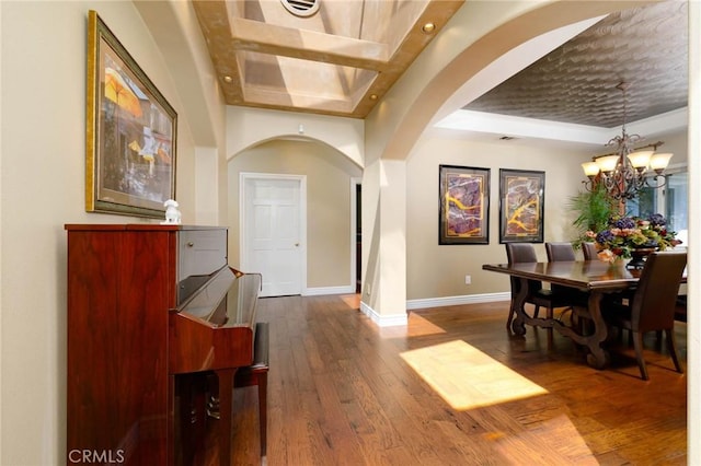 dining space featuring arched walkways, baseboards, dark wood-style floors, a notable chandelier, and a tray ceiling