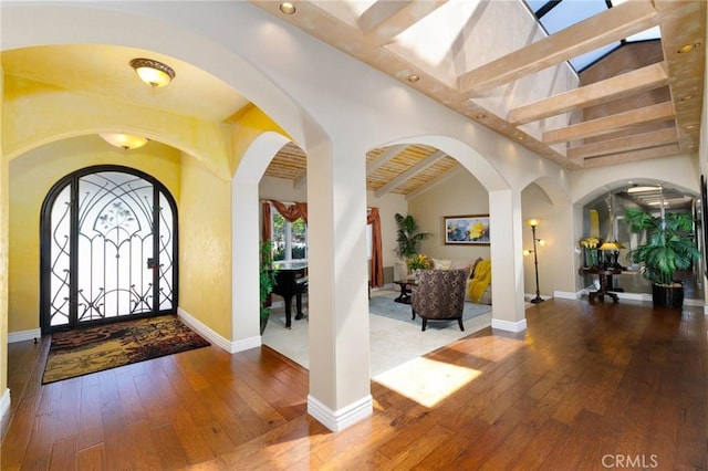 foyer with baseboards, beamed ceiling, hardwood / wood-style flooring, and arched walkways