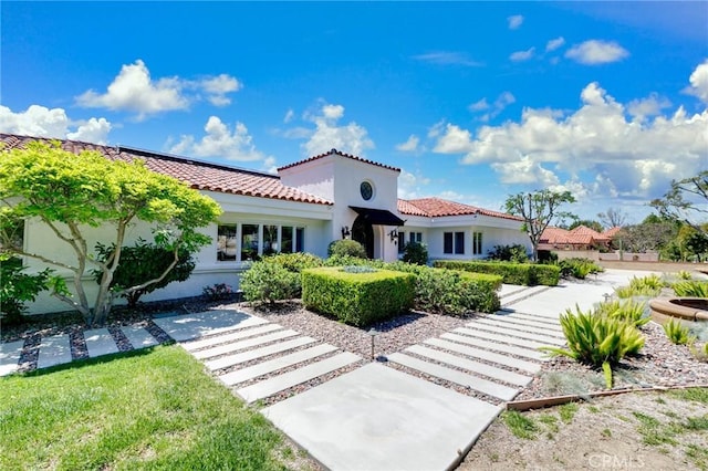 mediterranean / spanish-style house with stucco siding, solar panels, and a tile roof