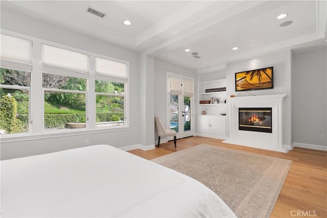 bedroom with a glass covered fireplace, baseboards, light wood-type flooring, and visible vents