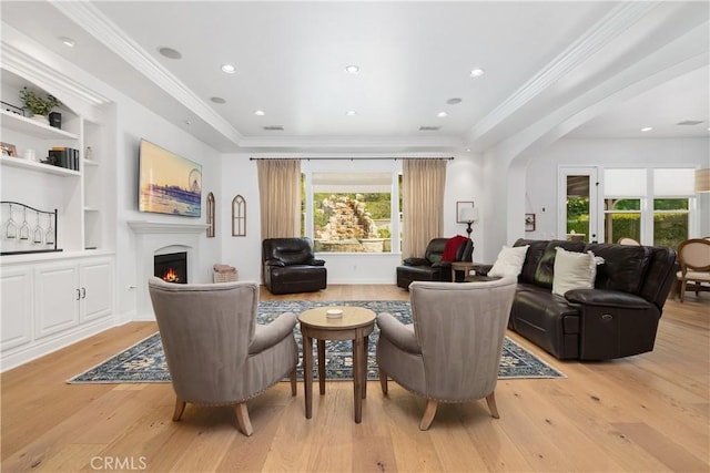 living room featuring crown molding, built in features, light wood-style floors, a lit fireplace, and arched walkways