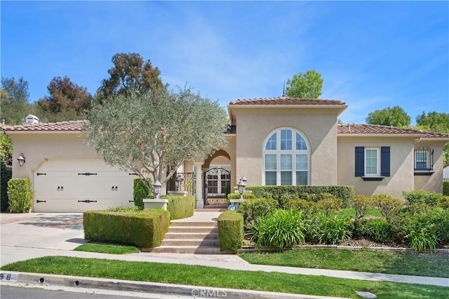 mediterranean / spanish home with a garage, stucco siding, driveway, and a tiled roof