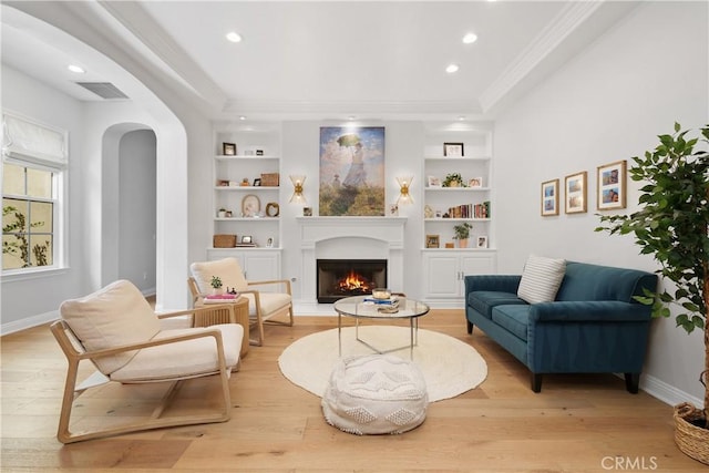 sitting room with a warm lit fireplace, light wood finished floors, built in features, baseboards, and visible vents