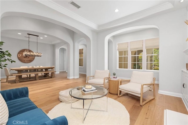 living area with visible vents, arched walkways, baseboards, light wood finished floors, and ornamental molding