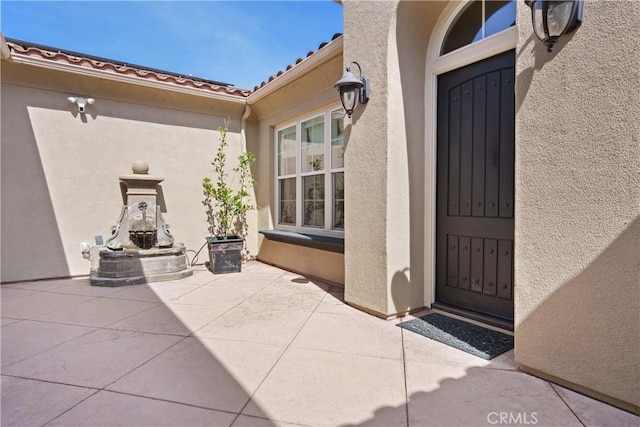 property entrance featuring a patio, stucco siding, and a tiled roof