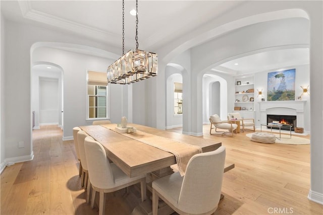 dining area featuring ornamental molding, recessed lighting, built in shelves, arched walkways, and light wood finished floors