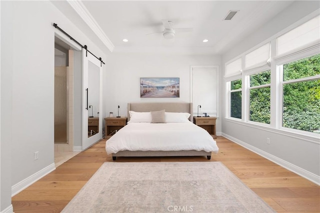 bedroom featuring visible vents, ornamental molding, baseboards, a barn door, and light wood finished floors