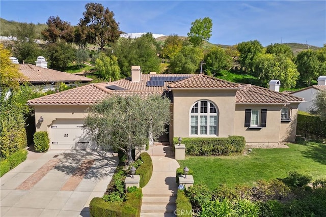 mediterranean / spanish house with driveway, a chimney, a tile roof, solar panels, and a front lawn