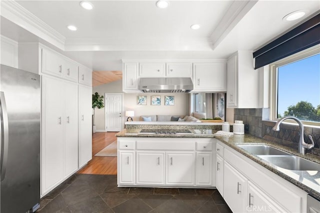 kitchen with a sink, freestanding refrigerator, a peninsula, black electric stovetop, and under cabinet range hood