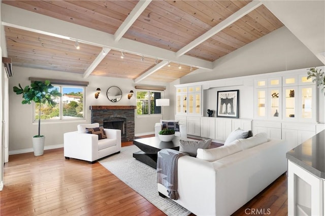 living area featuring baseboards, rail lighting, lofted ceiling with beams, and a fireplace