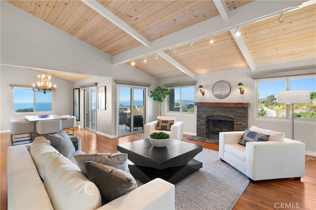 living area featuring a stone fireplace, rail lighting, wood finished floors, a chandelier, and vaulted ceiling with beams