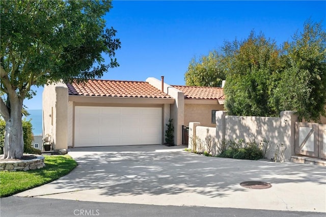 mediterranean / spanish house with fence, stucco siding, an attached garage, and a tile roof