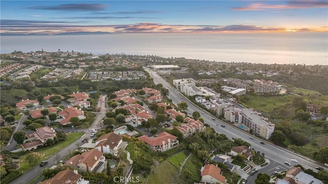 aerial view at dusk with a water view and a residential view
