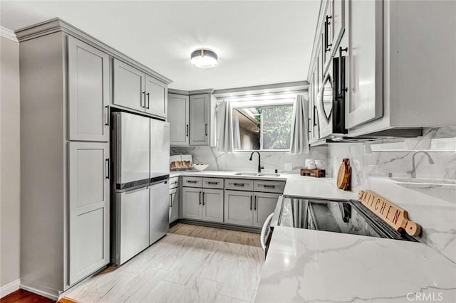 kitchen with freestanding refrigerator, a sink, gray cabinetry, and light stone countertops