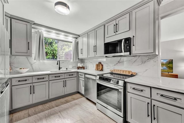 kitchen featuring a sink, gray cabinets, appliances with stainless steel finishes, and light stone countertops