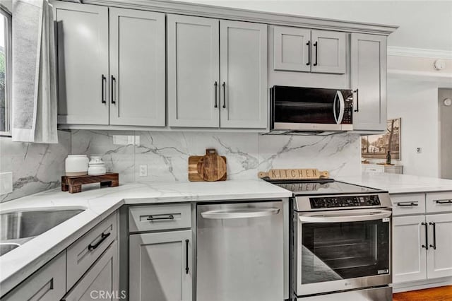 kitchen featuring gray cabinets, backsplash, stainless steel appliances, and light stone countertops