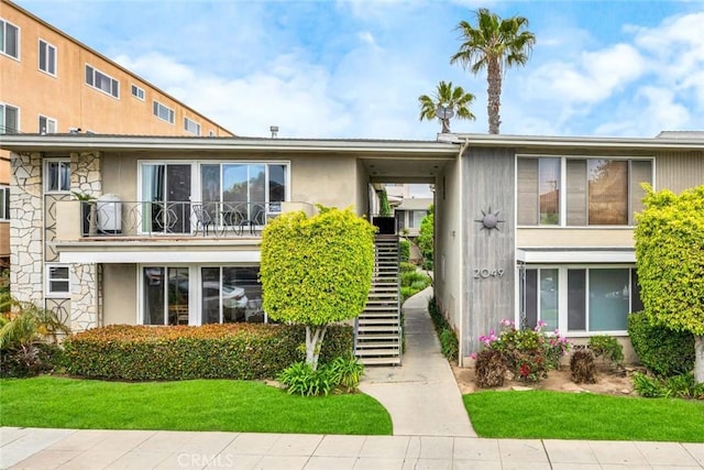 view of front of property featuring stairs, a front lawn, stucco siding, and stone siding