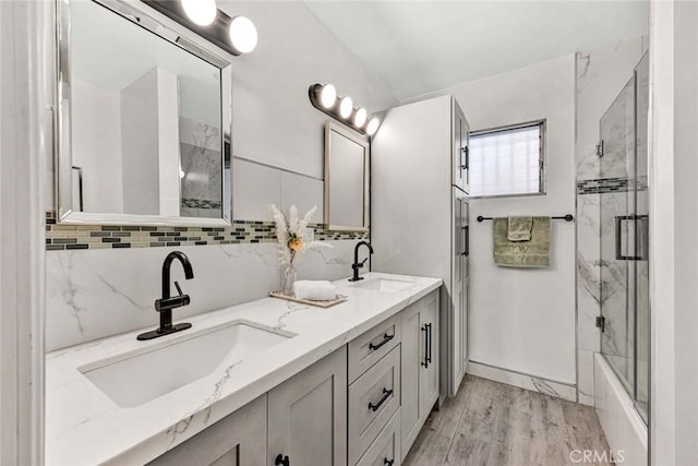 full bath featuring double vanity, a sink, wood finished floors, and bath / shower combo with glass door
