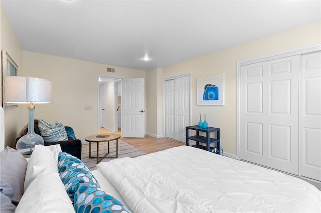 bedroom featuring visible vents, baseboards, multiple closets, and wood finished floors