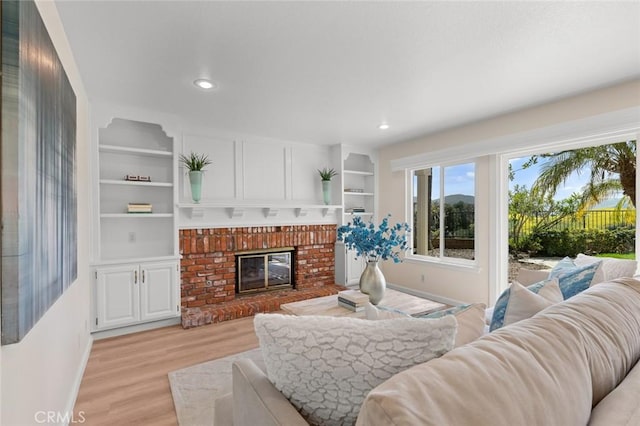 living room featuring baseboards, recessed lighting, light wood-style flooring, and a brick fireplace