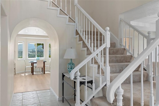 stairs featuring arched walkways, baseboards, and tile patterned flooring