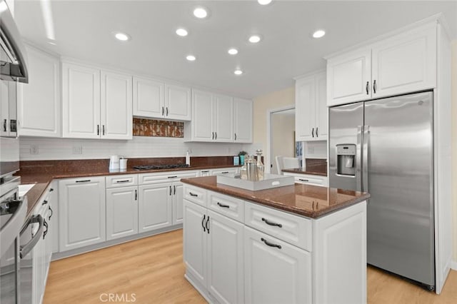 kitchen with gas cooktop, a kitchen island, white cabinets, stainless steel fridge, and light wood-style flooring