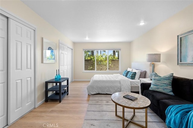 bedroom featuring two closets, recessed lighting, baseboards, and light wood-type flooring