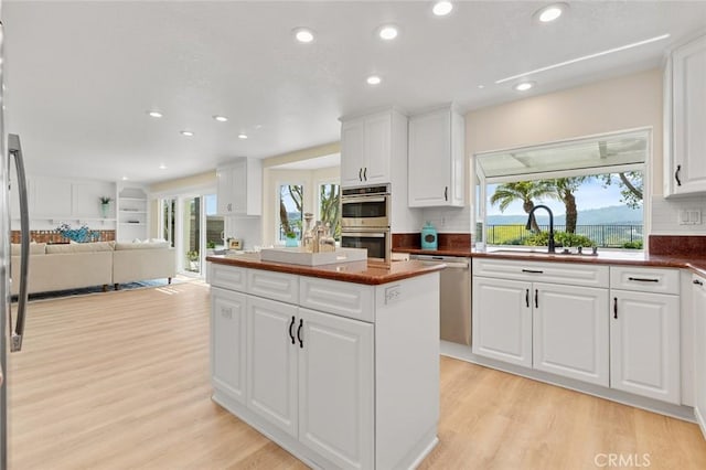 kitchen featuring a center island, white cabinets, a sink, light wood-style flooring, and stainless steel appliances
