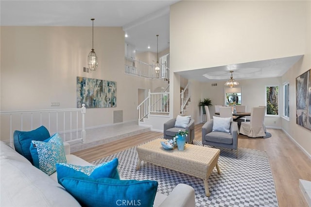 living room with visible vents, wood finished floors, baseboards, high vaulted ceiling, and stairway