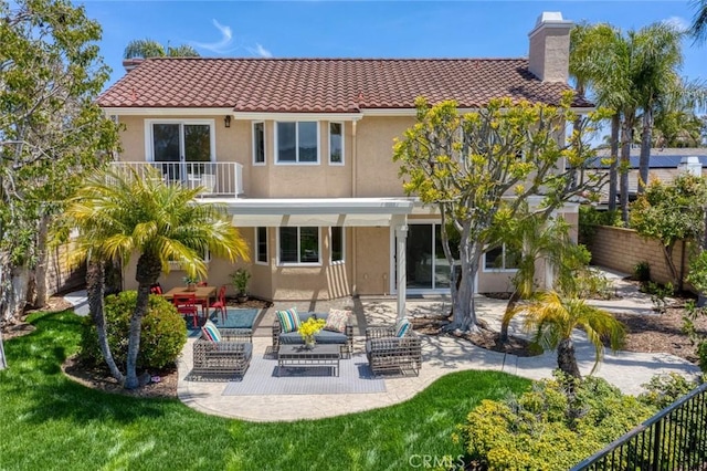 back of house with fence, a balcony, stucco siding, a chimney, and a patio area