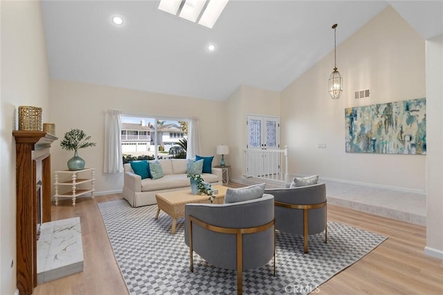 living room featuring visible vents, a skylight, high vaulted ceiling, baseboards, and light wood finished floors