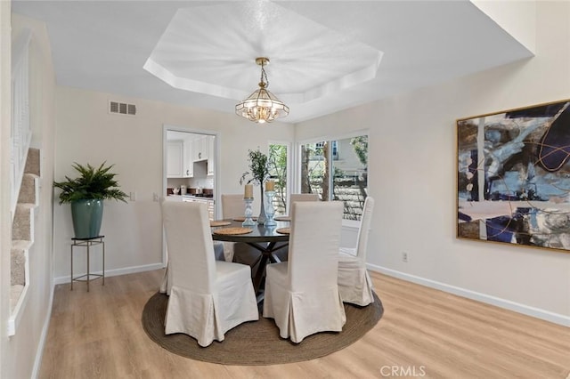 dining area featuring visible vents, a raised ceiling, a chandelier, and light wood-type flooring