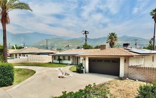 3915 Valencia Ave, San Bernardino, CA 92404 - ranch-style house with solar panels, fence, a mountain view, concrete driveway, and an attached garage