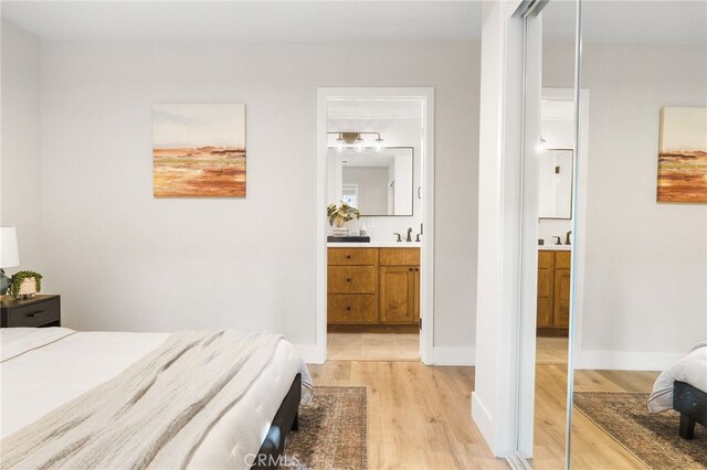 bedroom with light wood-type flooring, a sink, and connected bathroom