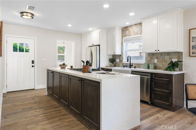 kitchen featuring wood finished floors, a sink, stainless steel appliances, white cabinetry, and a wealth of natural light