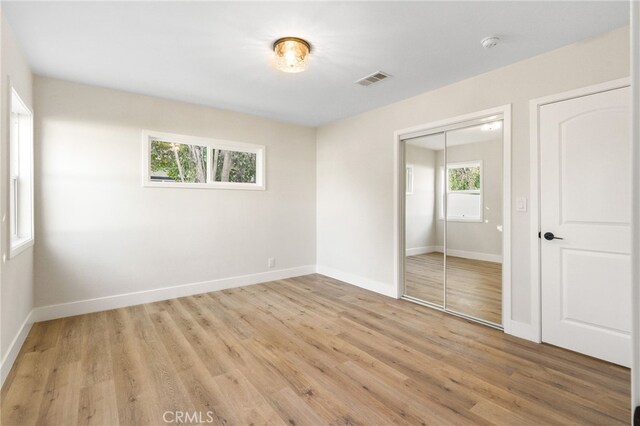 unfurnished bedroom with a closet, baseboards, visible vents, and light wood-style floors
