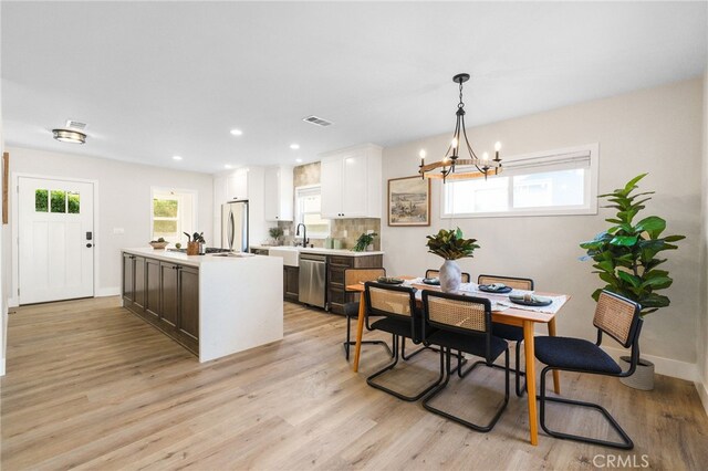 dining space featuring baseboards, visible vents, light wood finished floors, and a notable chandelier